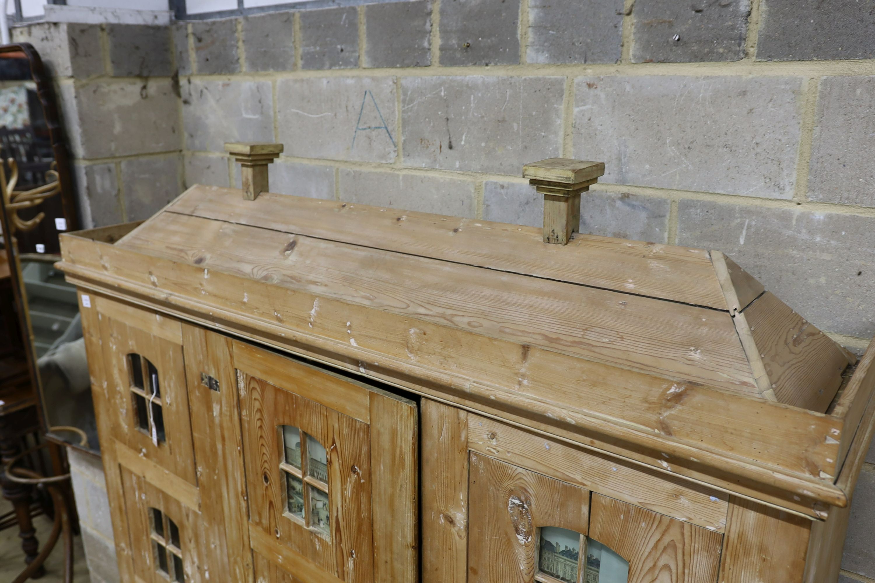 A 19th century stripped pine hall cupboard modelled as a dolls house the two door nine window facade enclosing a compartmented interior, width 182cm, depth 46cm, height 192cm